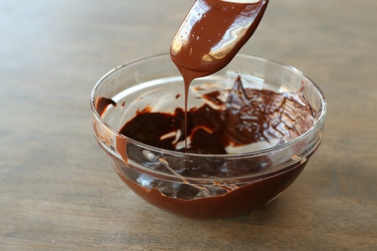 Melted chocolate dripping off a spoon into a glass bowl