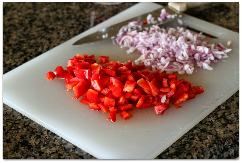 diced red pepper and finely diced onion on a cutting board with a knife
