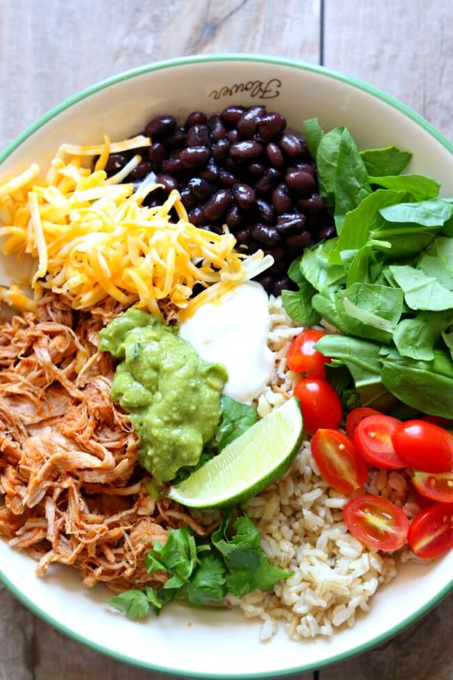 Slow Cooker Savory Pork Burrito Bowls--perfectly tender and shreddable 5 ingredient pork is cooked all day on low and slow in your crockpot and then served with rice, guacamole, black beans, sour cream and more of your favorite toppings.