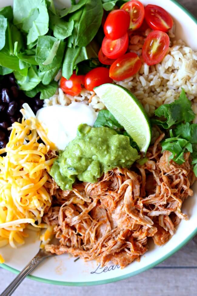 Instant Pot Burrito Bowls--perfectly tender and shreddable 5 ingredient pork is cooked quickly in your Instant Pot and then served with rice, guacamole, black beans, sour cream and more of your favorite toppings.