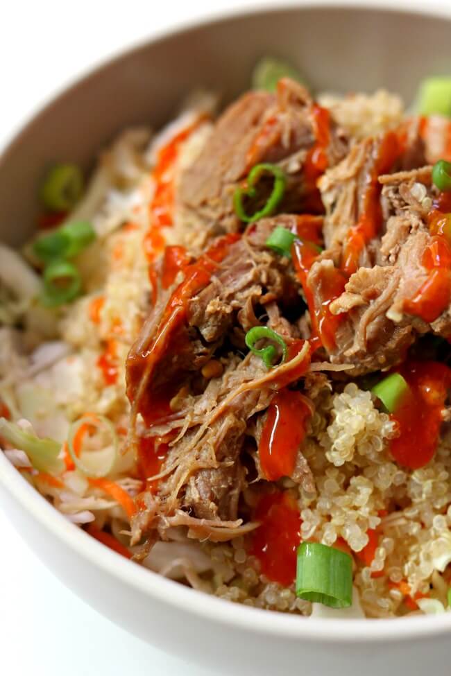 Slow Cooker Pork Quinoa Cabbage Bowls--pork is cooked until fork tender with chili garlic sauce and a secret ingredient. The meat is added to a bowl with shredded cabbage, quinoa, diced green onions and finally topped with a drizzle of sriracha. This makes a beautiful and delicious summer meal. 