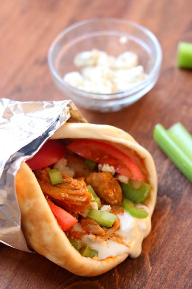 Slow Cooker Buffalo Chicken Gyros--bleu cheese dressing is spooned down the middle of a warm pita and then topped with shredded chicken that has been stirred together with buffalo sauce. Then it's topped with crunchy celery and bleu cheese crumbles.  This is a party in your mouth!