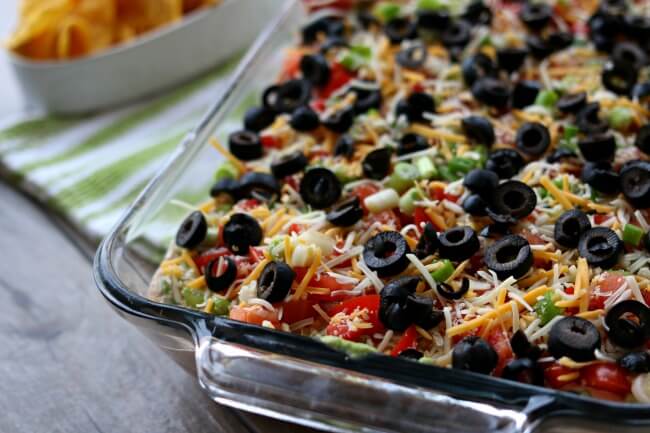 7 Layer Dip--this is the best 7 layer dip I have ever eaten! It starts with a layer of perfectly seasoned homemade refried beans (which you can make in the Instant Pot or slow cooker), then a layer of sour cream mixed with taco seasoning and salsa, next a layer of smashed avocados seasoned with lime juice and finally it's topped with diced tomatoes, green onions, cheese and olives. Every layer comes together in perfect harmony on top of a tortilla chip and popped into your mouth.