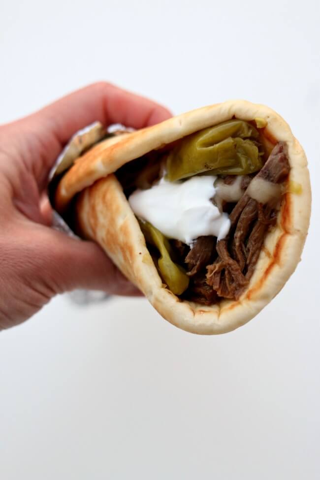 Slow Cooker Mississippi Roast Gyros--tender shredded beef that has been cooked in pepperoncini juice is piled into a soft pita and then topped with monterey jack cheese and a dollop of sour cream. 