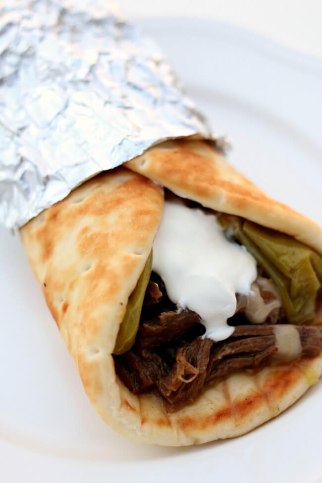 Instant Pot Mississippi Roast Gyros--tender shredded beef that has been cooked in pepperoncini juice is piled into a soft pita and then topped with monterey jack cheese and a dollop of sour cream. 