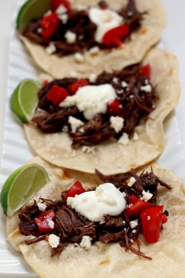 Slow Cooker Shredded Beef Street Tacos--small tortillas are piled with tender shredded seasoned beef, sour cream, tomatoes, cotija cheese and a squeeze of lime. The beef is cooked low and slow and becomes super tender in a over many hours. 