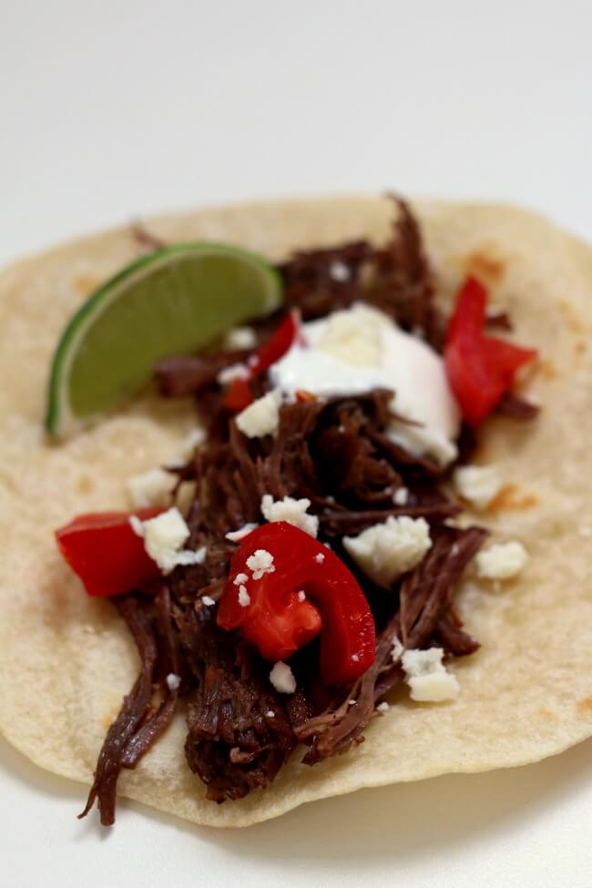 Slow Cooker Shredded Beef Street Tacos--small tortillas are piled with tender shredded seasoned beef, sour cream, tomatoes, cotija cheese and a squeeze of lime. The beef is cooked low and slow and becomes super tender in a over many hours. 