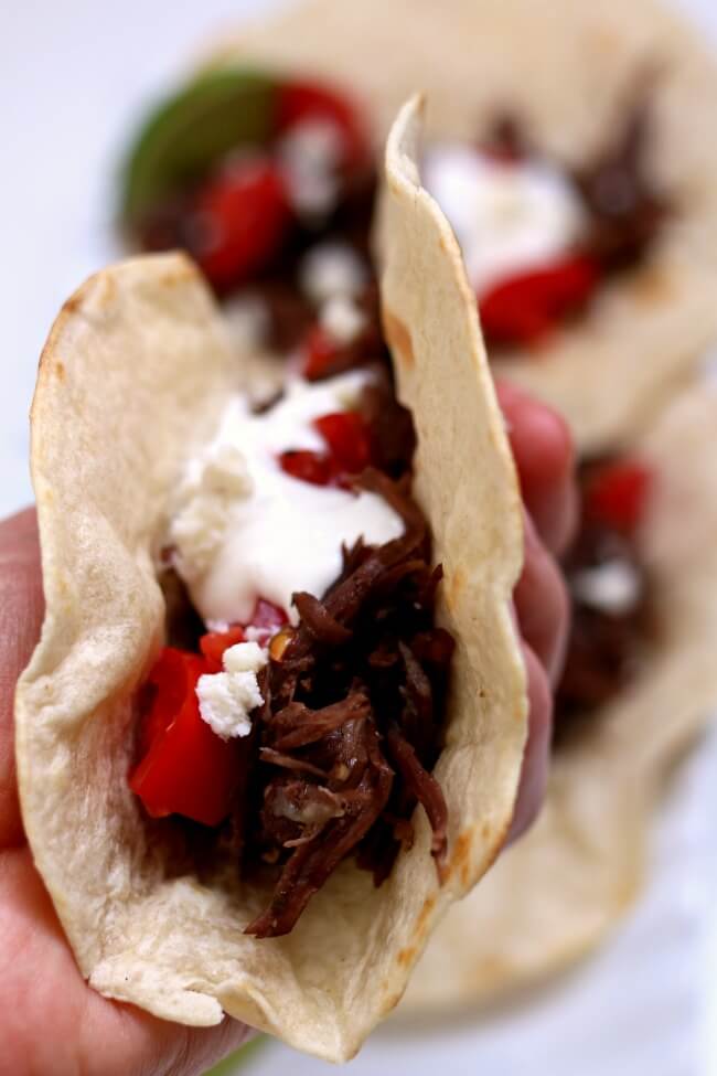 Instant Pot Shredded Beef Street Tacos--small tortillas are piled with tender shredded seasoned beef, sour cream, tomatoes, cotija cheese and a squeeze of lime. The beef is made in an electric pressure cooker and becomes super tender in a matter of minutes. 