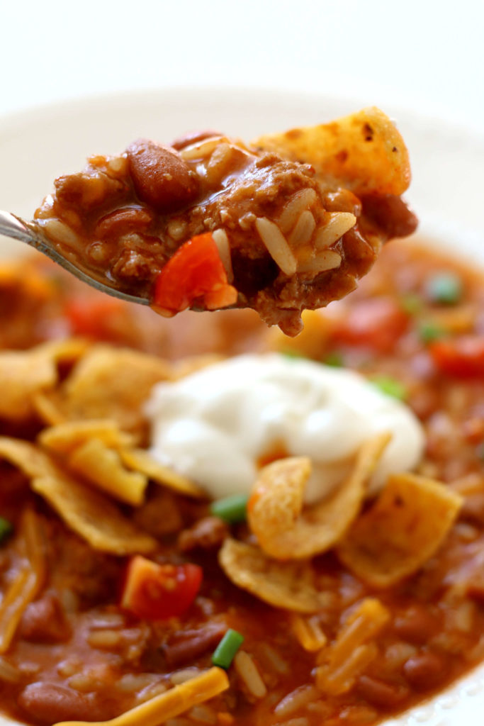 A spoon with chili and fritos on top