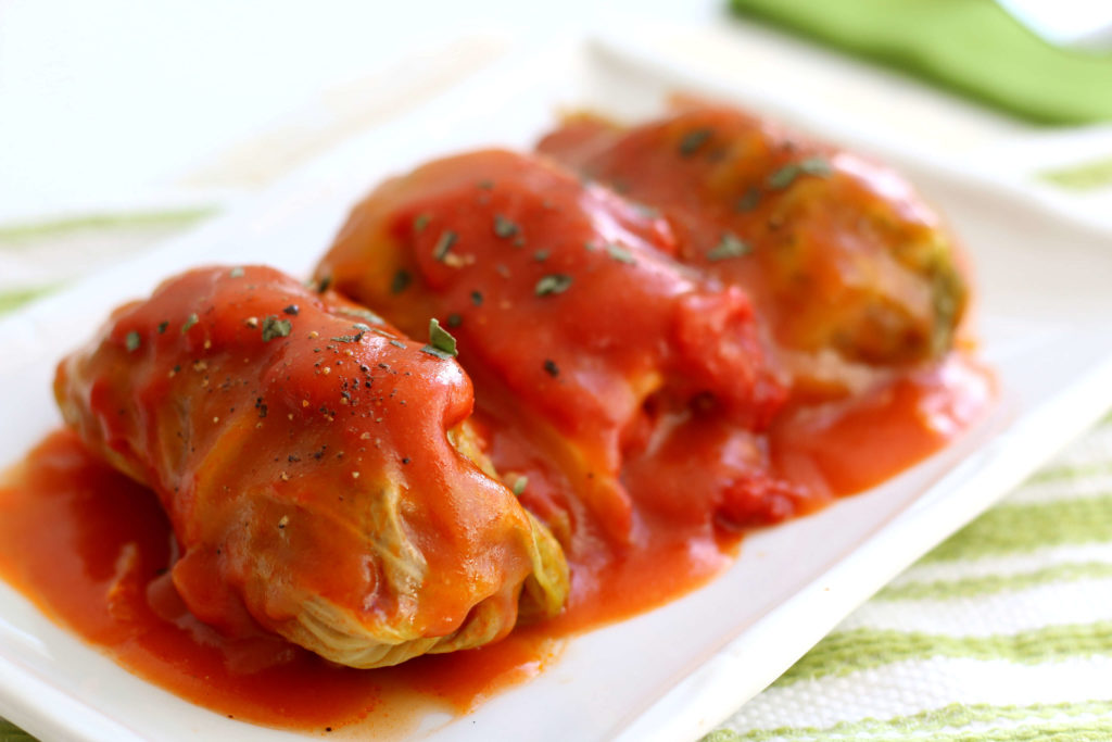 3 cabbage rolls with red sauce on a white plate