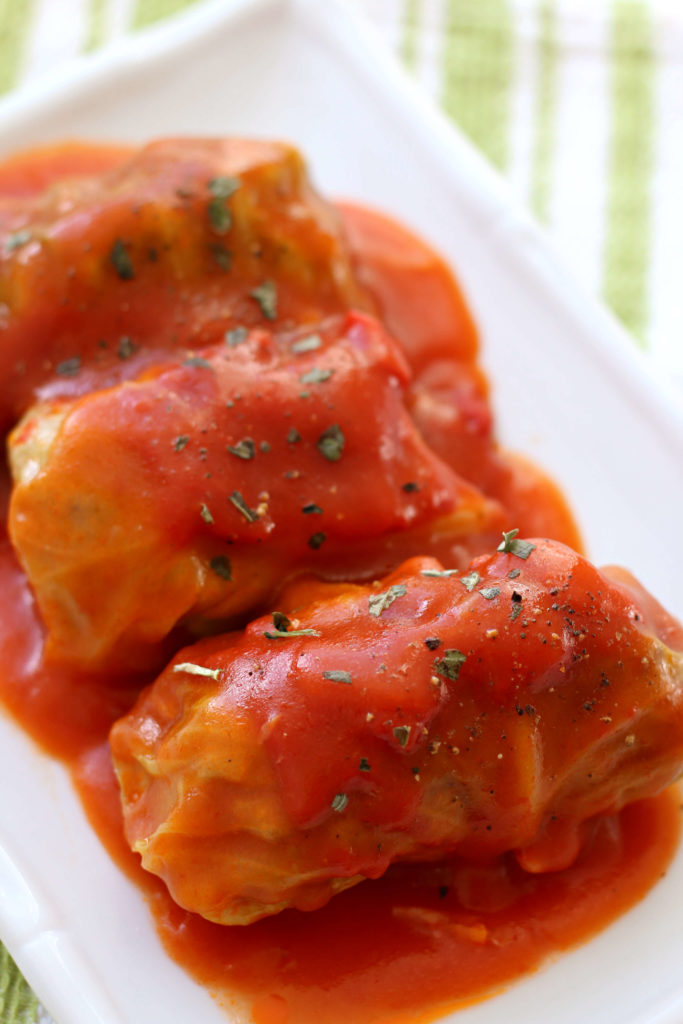 3 cabbage rolls with red sauce on a white plate