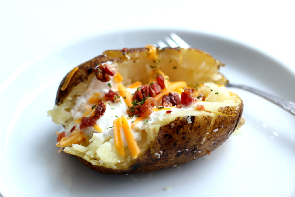baked potato with cheese, sour cream and bacon on a white plate