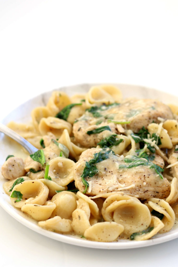 chicken, pasta and spinach on a white plate 