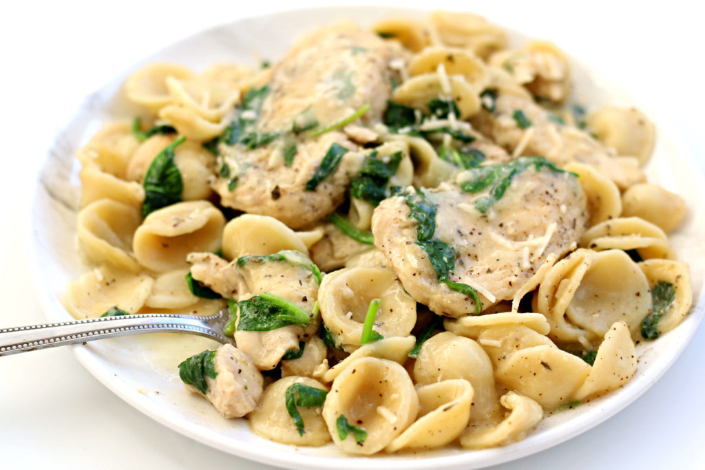 chicken, pasta and spinach on a white plate 