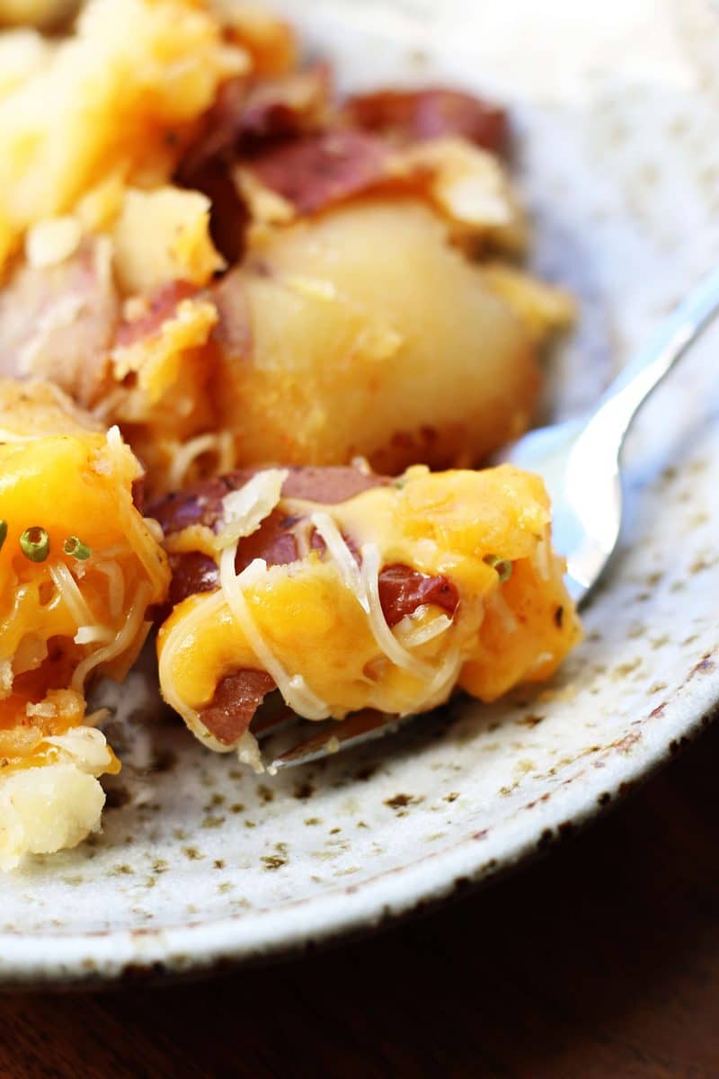 Slow Cooker Smashed Potato Bake--tender red potatoes coated in butter, garlic and seasonings, lightly smashed and finished with melted cheddar and Parmesan cheese.